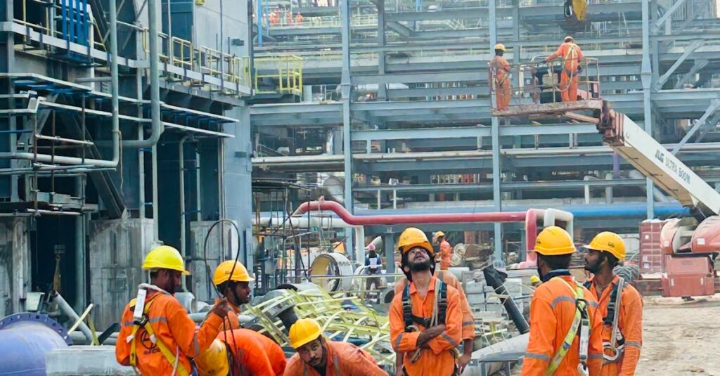 Group of construction workers in orange uniforms operating at an industrial site.