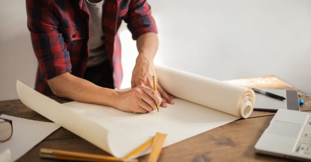 A focused architectural designer drafting blueprints at a desk indoors.